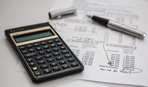 a black calculator, a black pen and a piece of paper